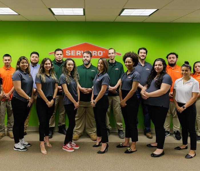Group of SERVPRO employees wearing SERVPRO polo shirts smiling, standing against a green wall with the SERVPRO logo.