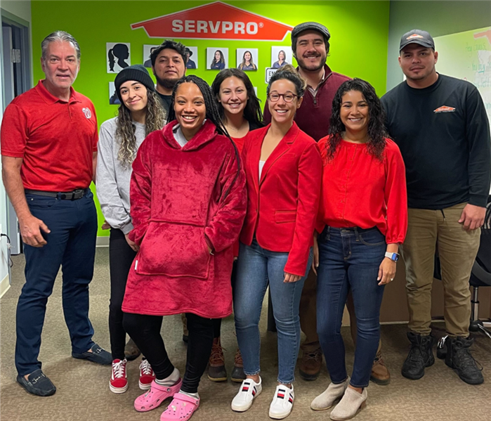 Eight SERVPRO employees wearing red in an office with the SERVPRO logo on the wall behind them